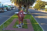 A sculpture of a red bull in a small-town median strip. A palm tree is behind.