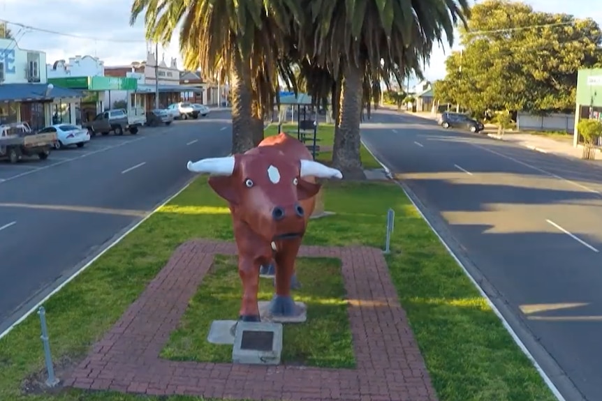 A sculpture of a red bull in a small town median strip. A plam tree is behind.