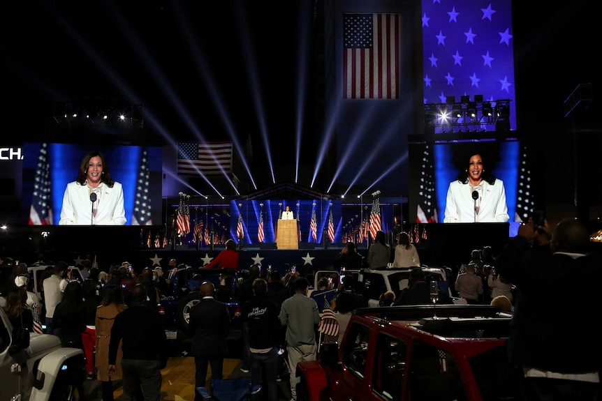 Kamala Harris speak at the podium, either side of her are big screens.