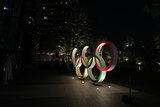 Two-metre high Olympic rings lit up in an urban park in the dark of the night. 