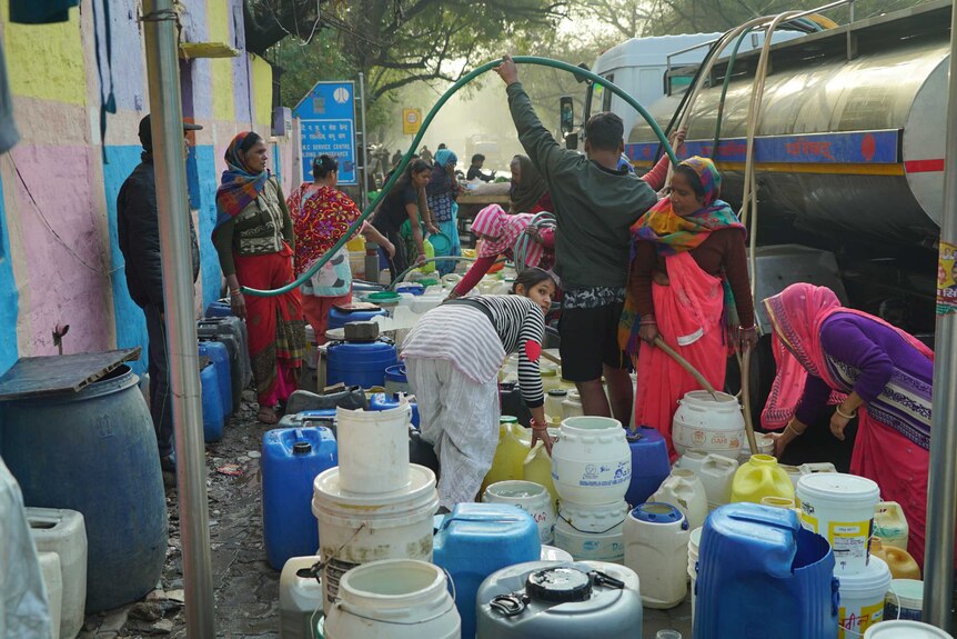 Locals fill up water containers with hoses pulled from a water truck.