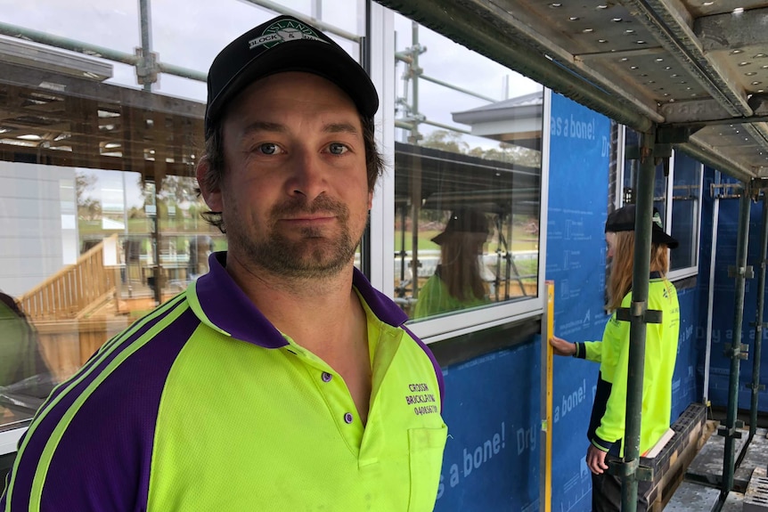 Bricklayer Andrew Crossin smiles at the camera, Chelsea is in the background