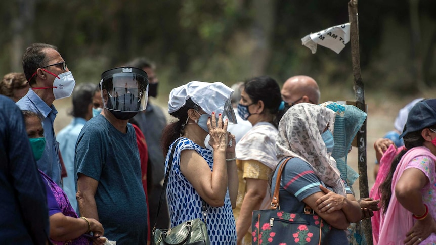 People wear masks, queue in the heat to get vaccinated in Mumbai. A man wears a face shield, a woman holds cloth over her head.