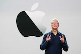 Tim Cook stands in front of a screen with an Apple logo.