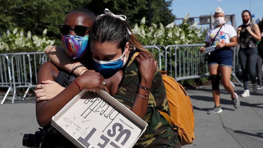 Two African American protesters hug holding a sign saying 'let us breathe'