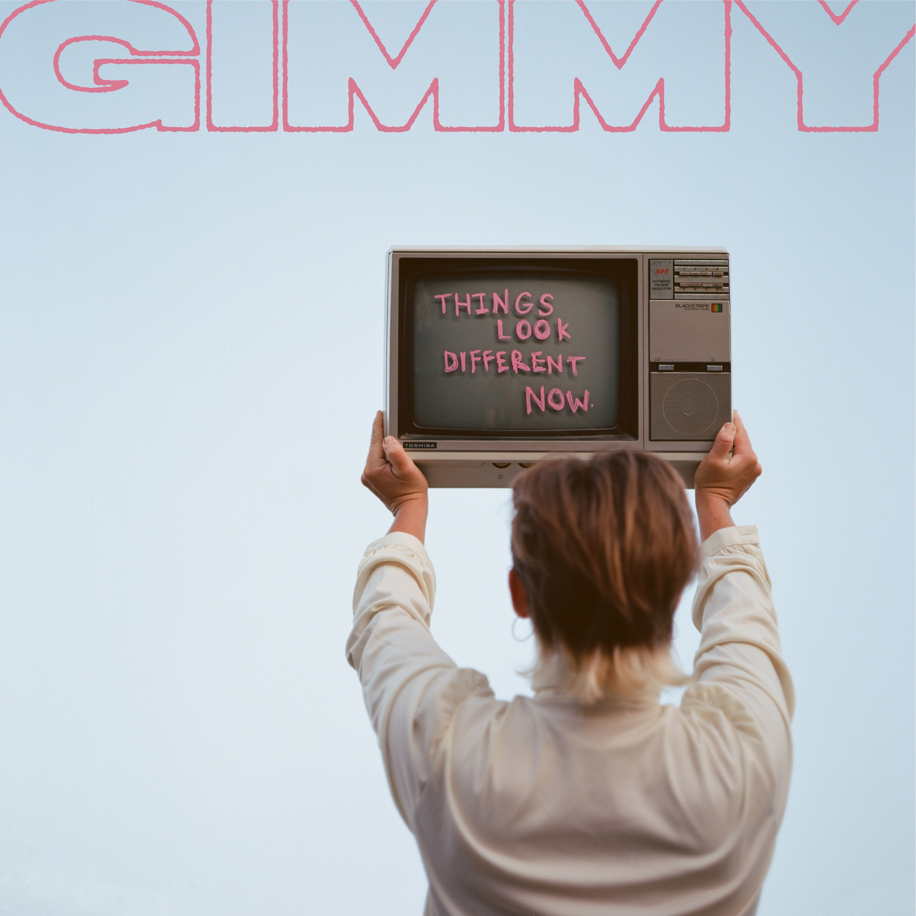 Woman with short, balayge hair stands with her back to camera, holding up a TV with text written on screen