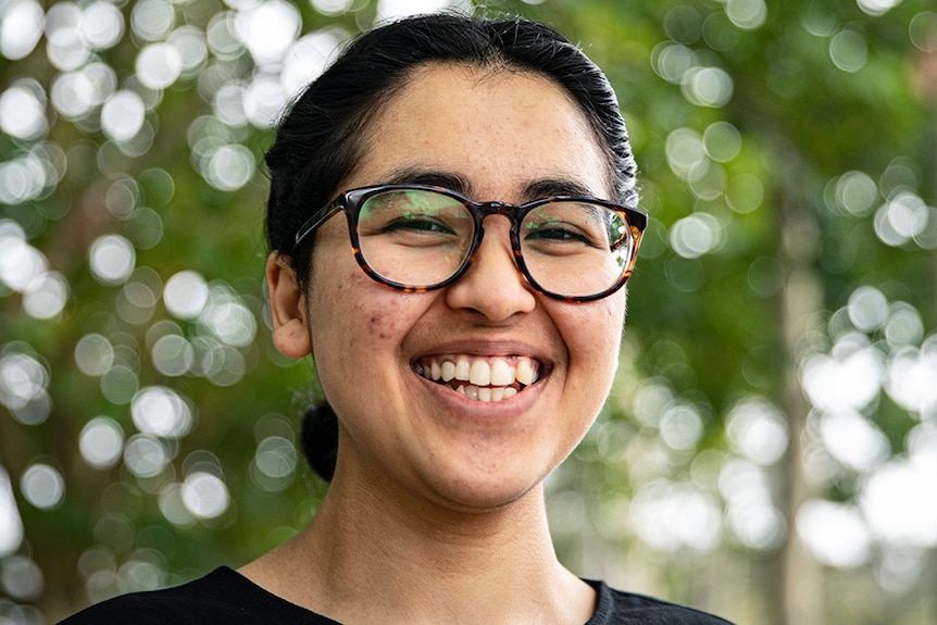 Dinita Rishal wearing glasses, with trees in background.