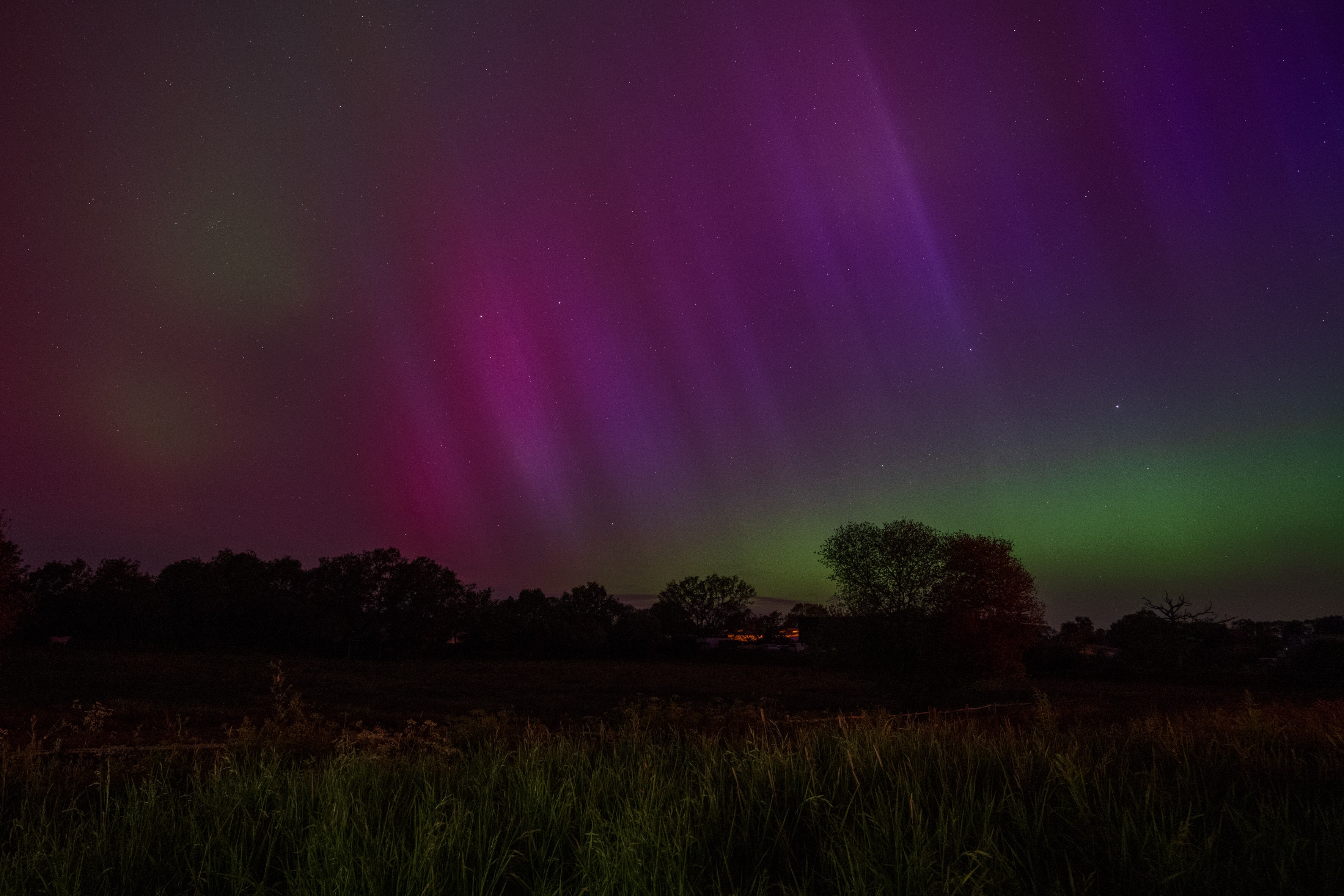 A farm land at night with the sky lit hues of green and pink.