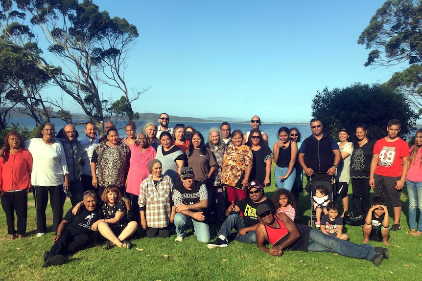 A group of people stand and sit on a lawn.