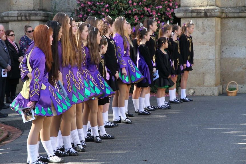 A line of dancers in traditional Irish dress lined up outside a church.