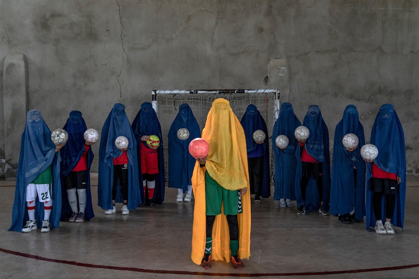 An Afghan women's soccer team poses for a photo wearing burqas and holding footballs.