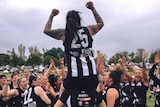 A woman with tattoos sits on a woman's shoulders at the football as they celebrate.