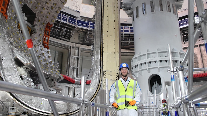 Dr Wauters in hard hat and high vis smiling with the first sector module installed in the pit behind him