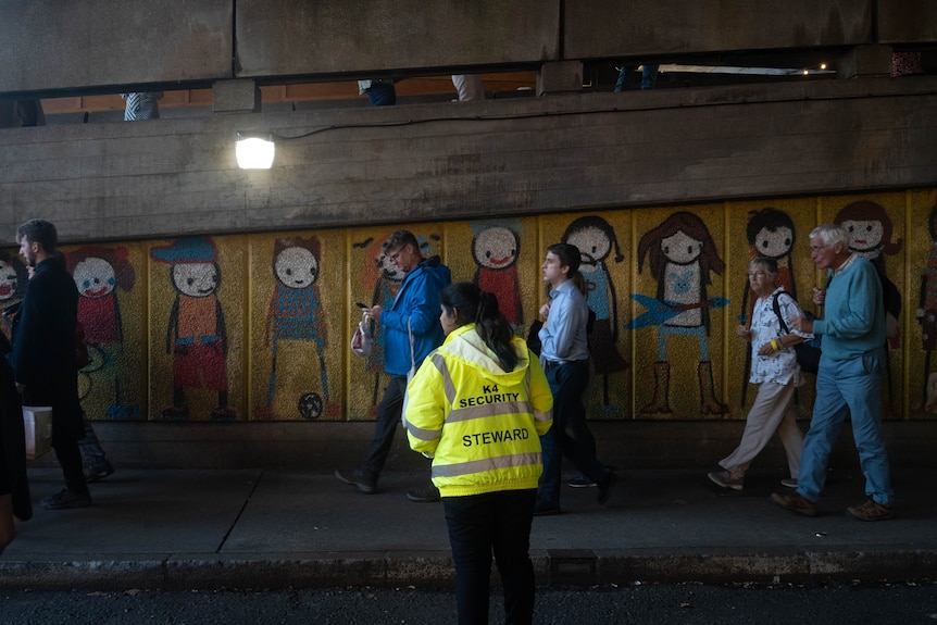 A steward watches a queue of people in a tunnel