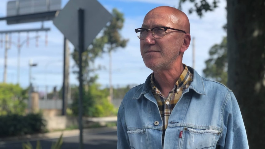 Man wearing a denim jacket and glasses standing outside.