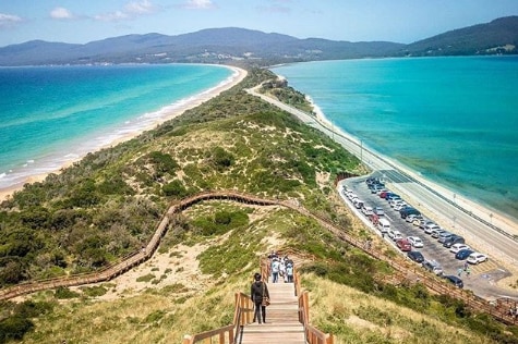 People walk down a wooden staircase to get to the beach on a thin stretch of Bruny Island