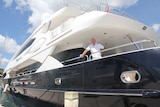 A man stands on the deck of a large yacht