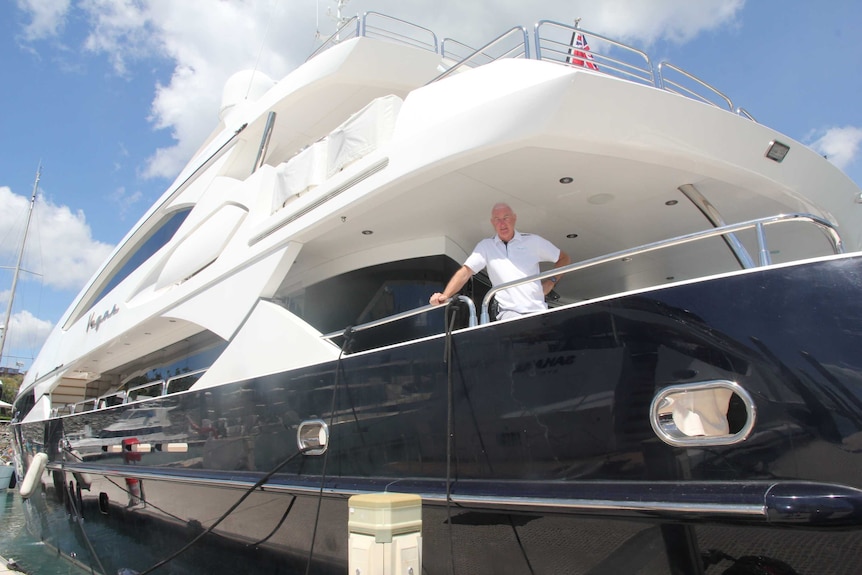 A man stands on the deck of a large yacht