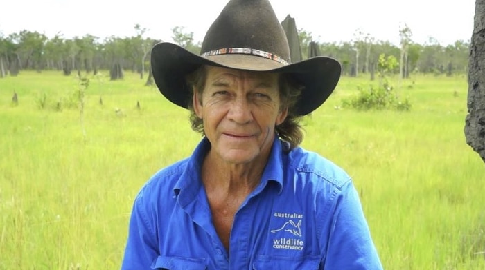 Graham Woods crouched down in front of a bright green grassy plain at Piccaninny Plains on Cape York