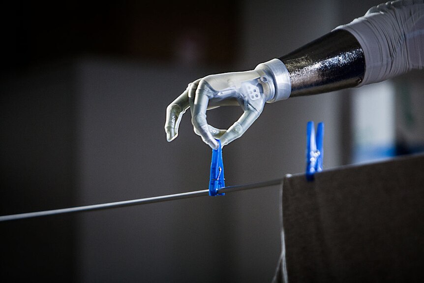 A bionic arm putting a peg on a clothesline