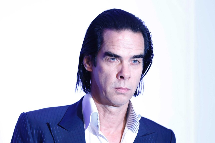 Nick Cave stands in front of a white screen