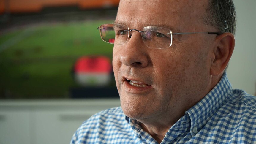 A tight head shot of a middle-aged man wearing spectacles talking during an interview indoors and looking off camera.