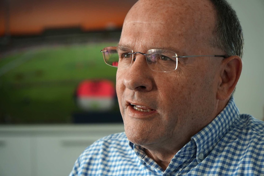 A tight head shot of a middle-aged man wearing spectacles talking during an interview indoors and looking off camera.
