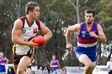 A Huntly footballer prepares to kick as he's chased by a North Bendigo player.