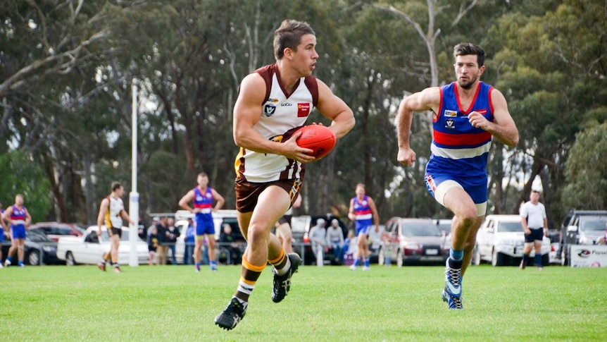 A Huntly footballer prepares to kick as he's chased by a North Bendigo player.