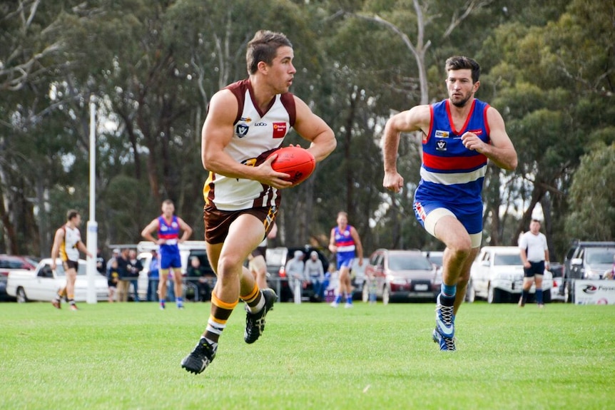 A Huntly footballer prepares to kick as he's chased by a North Bendigo player.