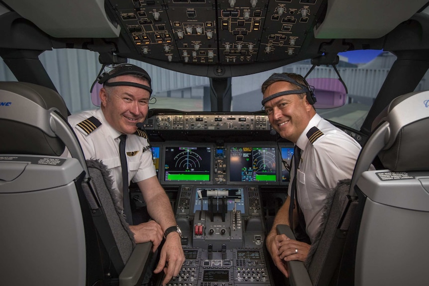 Both men sit in the cockpit of a Qantas plane.
