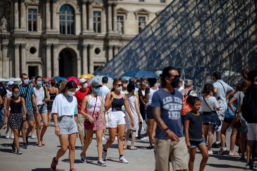 People walk past the Louvre Museum in Paris wearing masks.