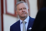 Anthony Albanese looks concerned, the walls of a church stand out of focus behind him.