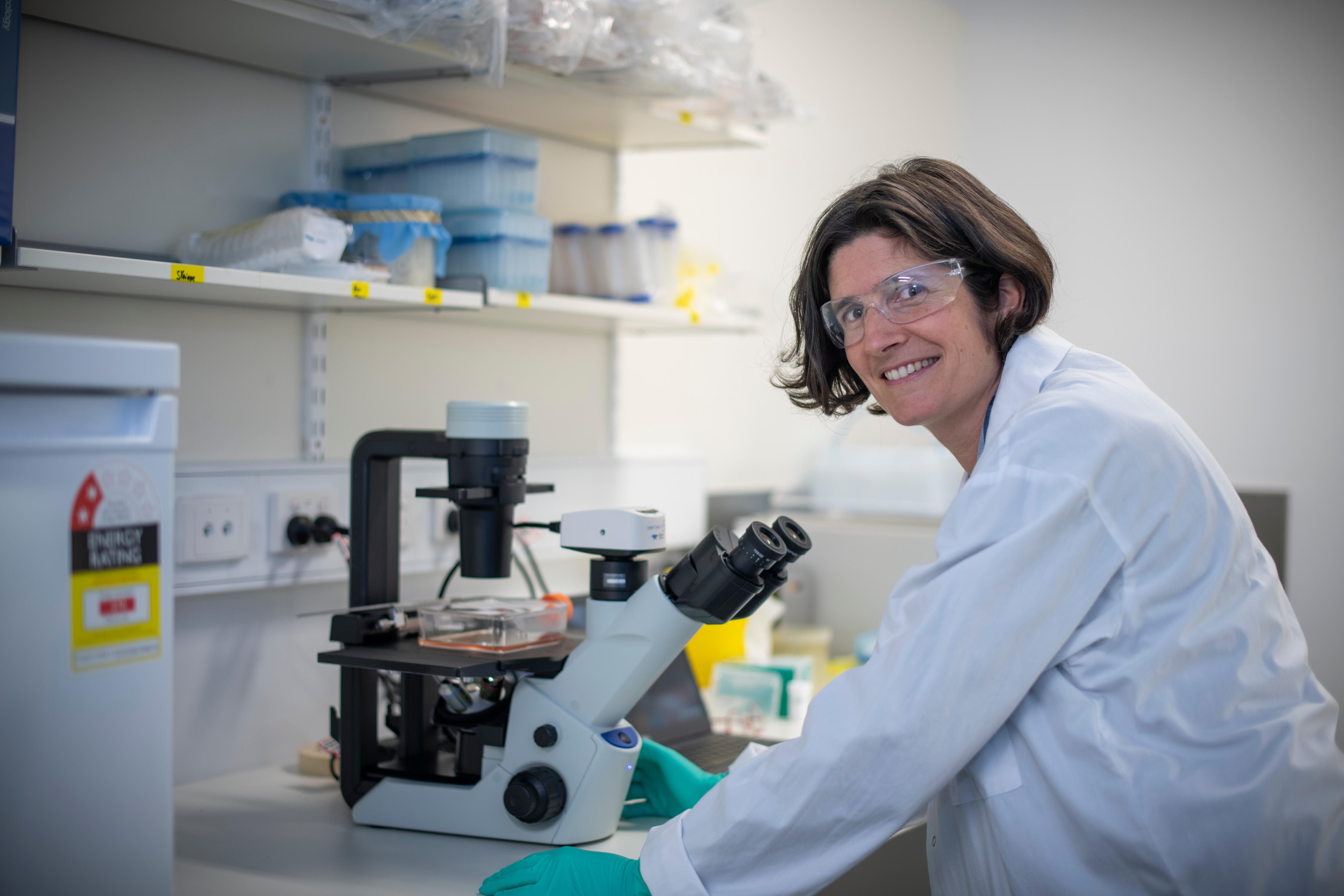 A woman wears a lab coat and glasses. 