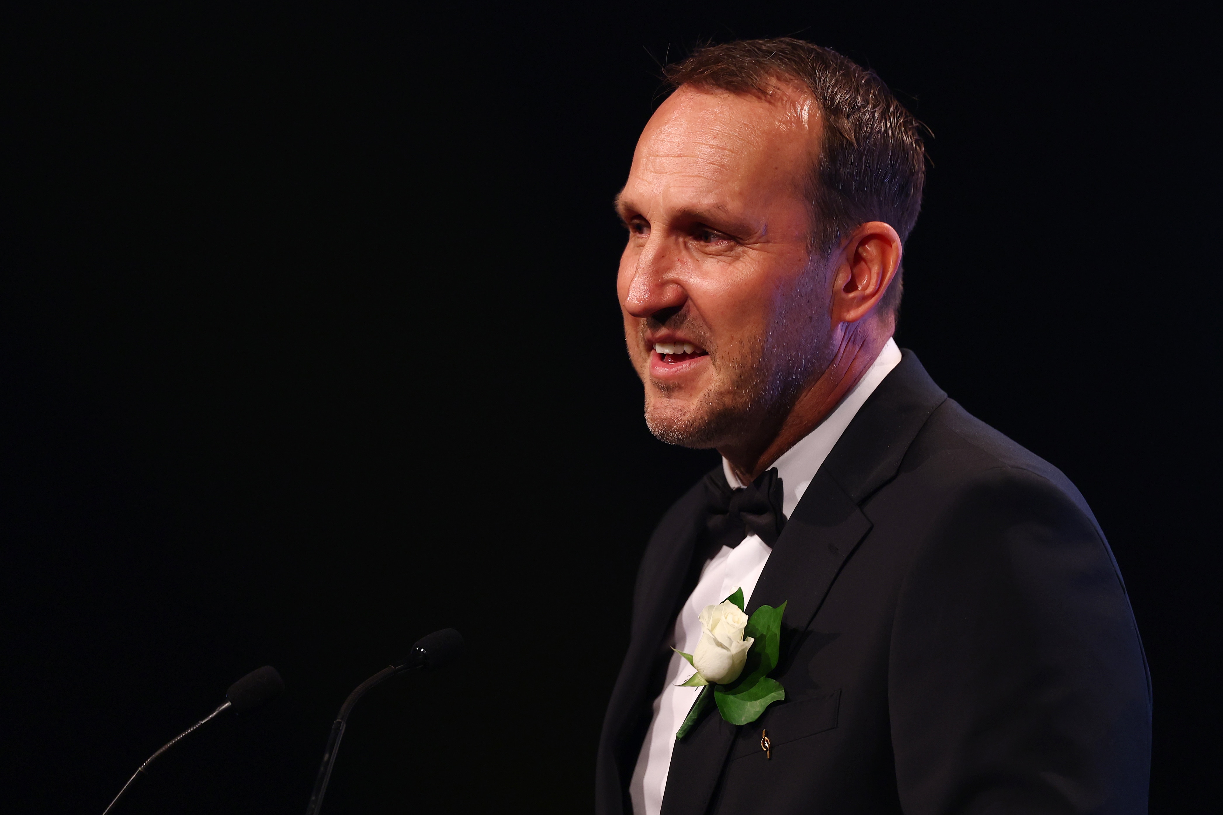Mark in a suit giving an address at an award ceremony, black tie.