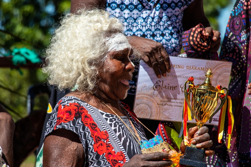 A happy woman holds a gold trophy and smiles.