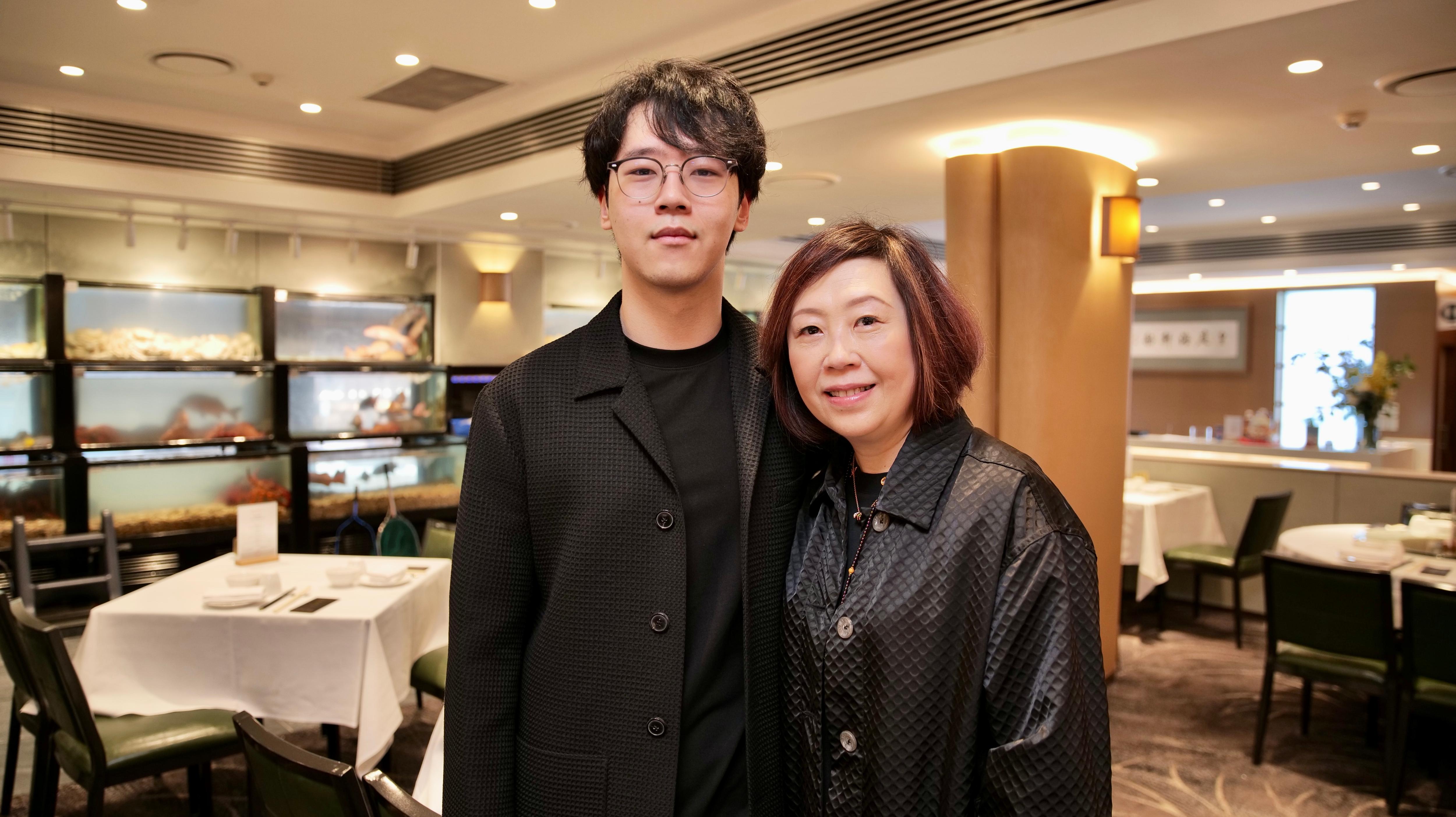 A young man and his mother stand next to each other inside a restaurant.