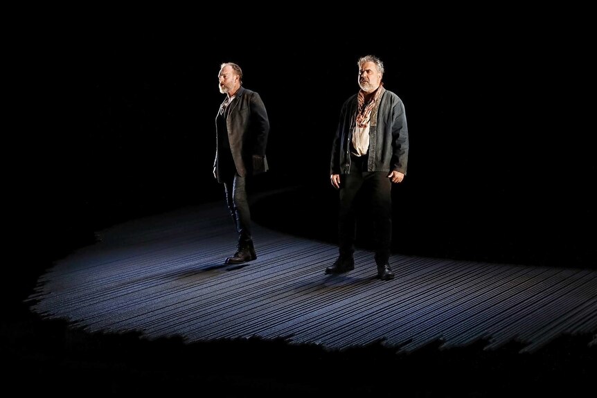 Hugo Weaving (left) and Wayne Blair (right) lit up on an empty stage, surrounded by darkness.