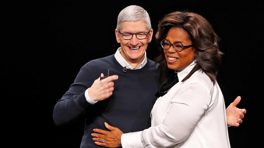 Tim Cook, CEO of Apple, and Oprah Winfrey hug on stage at an Apple event