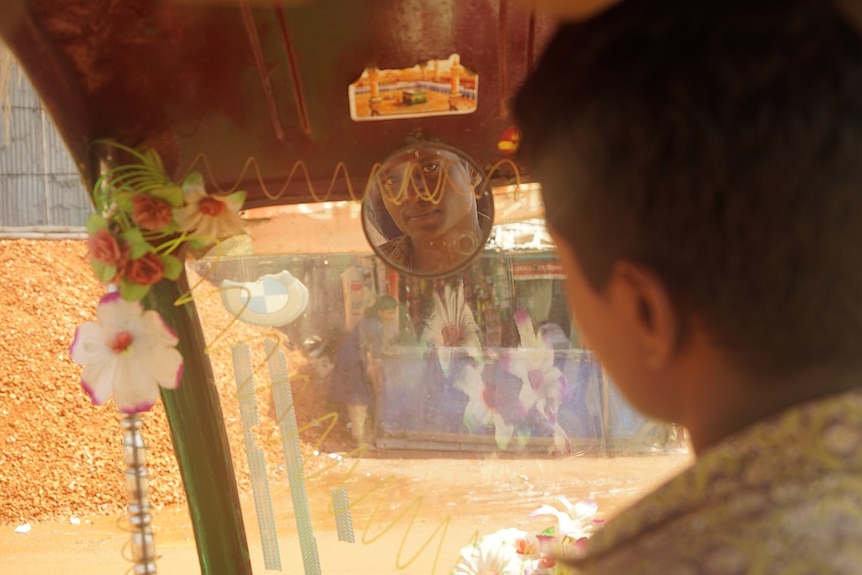 Saiful Islam sits in his tuk tuk looking in the rear view mirror.