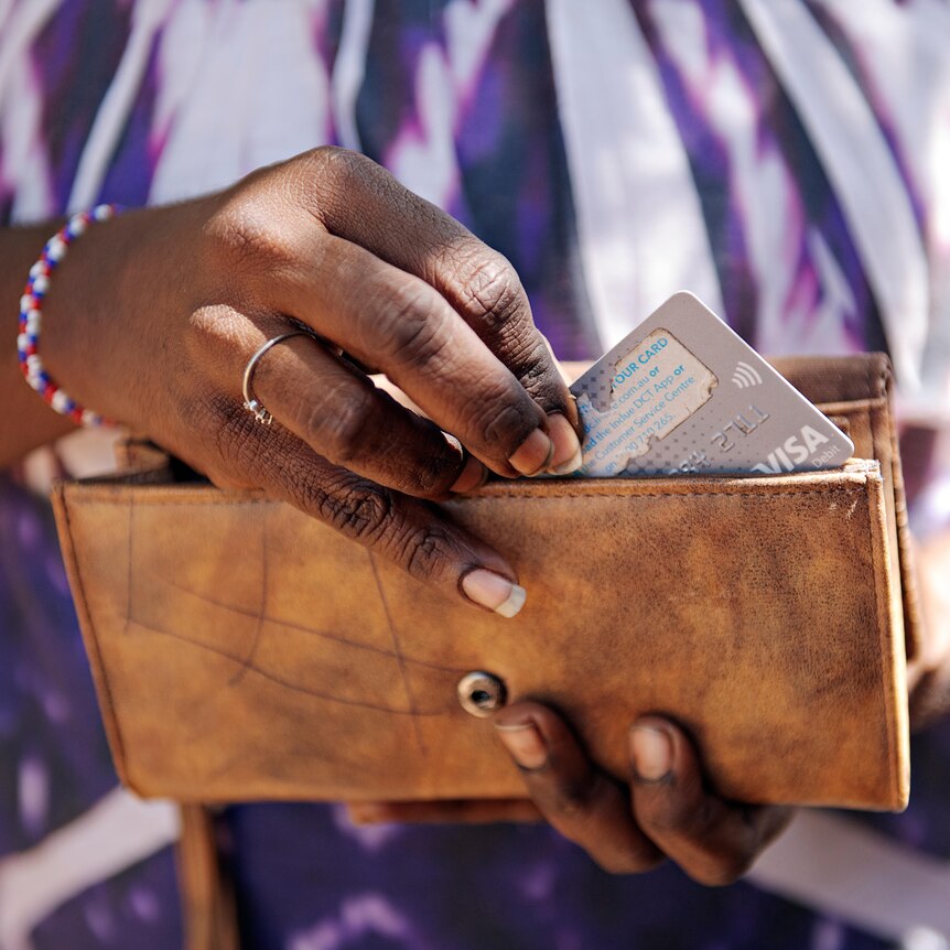 A woman puts a cashless debit card in a brown wallet