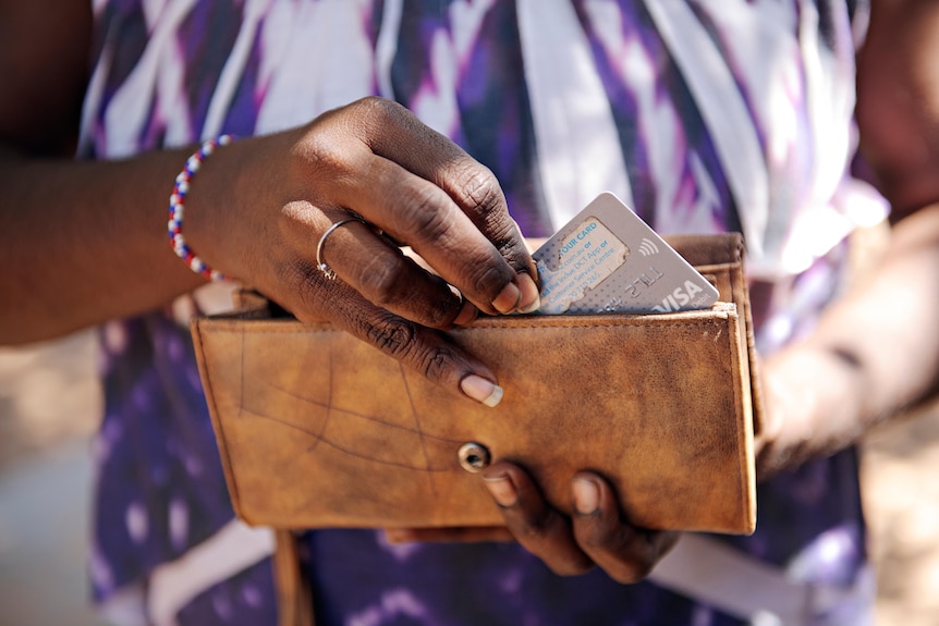 A woman puts a cashless debit card in a brown wallet