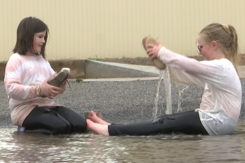 Two girls play, one pouring water from her shoe.