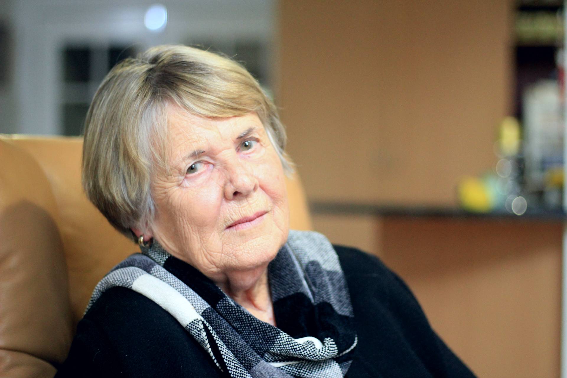 A fair-skinned woman who is aged 80, has fair hair, and a black jumper.  It's just her face de ella-she has a serious expression