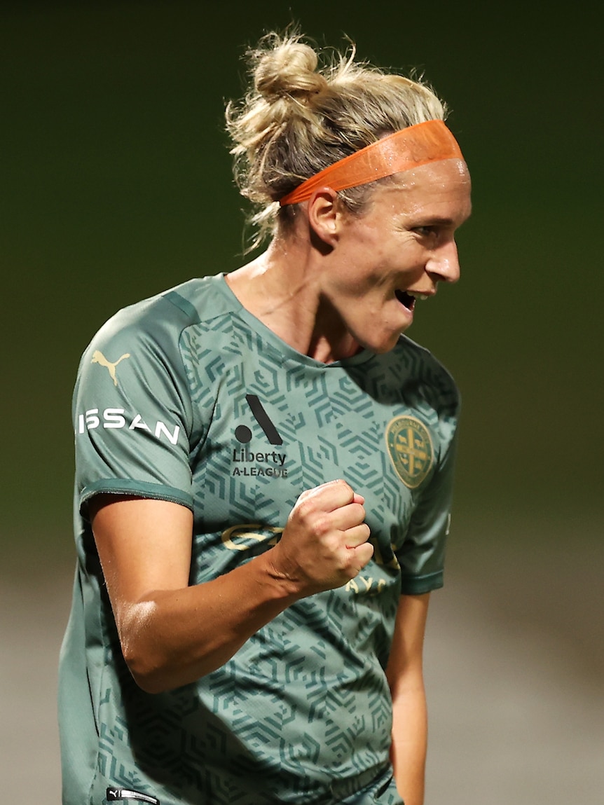 A soccer player wearing a green-grey top pumps her first