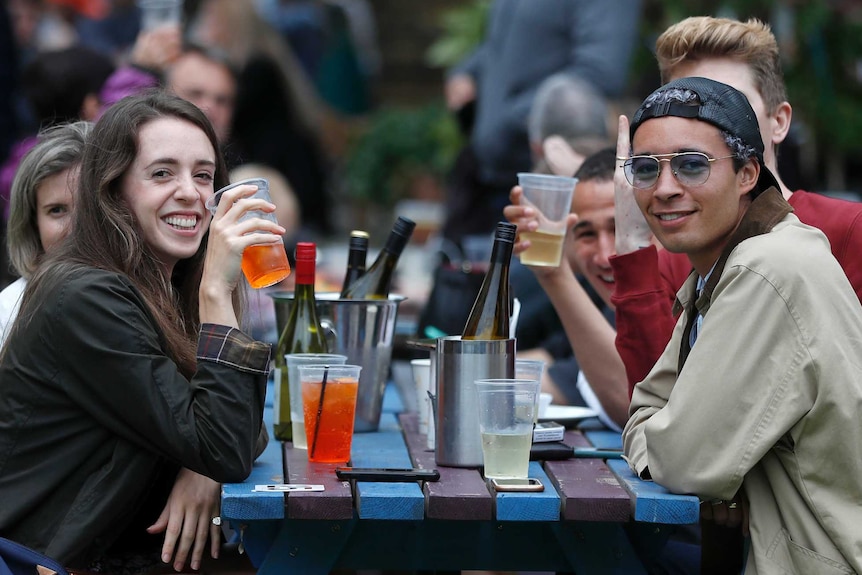 Group of friends sit outside drinking beers and cider.