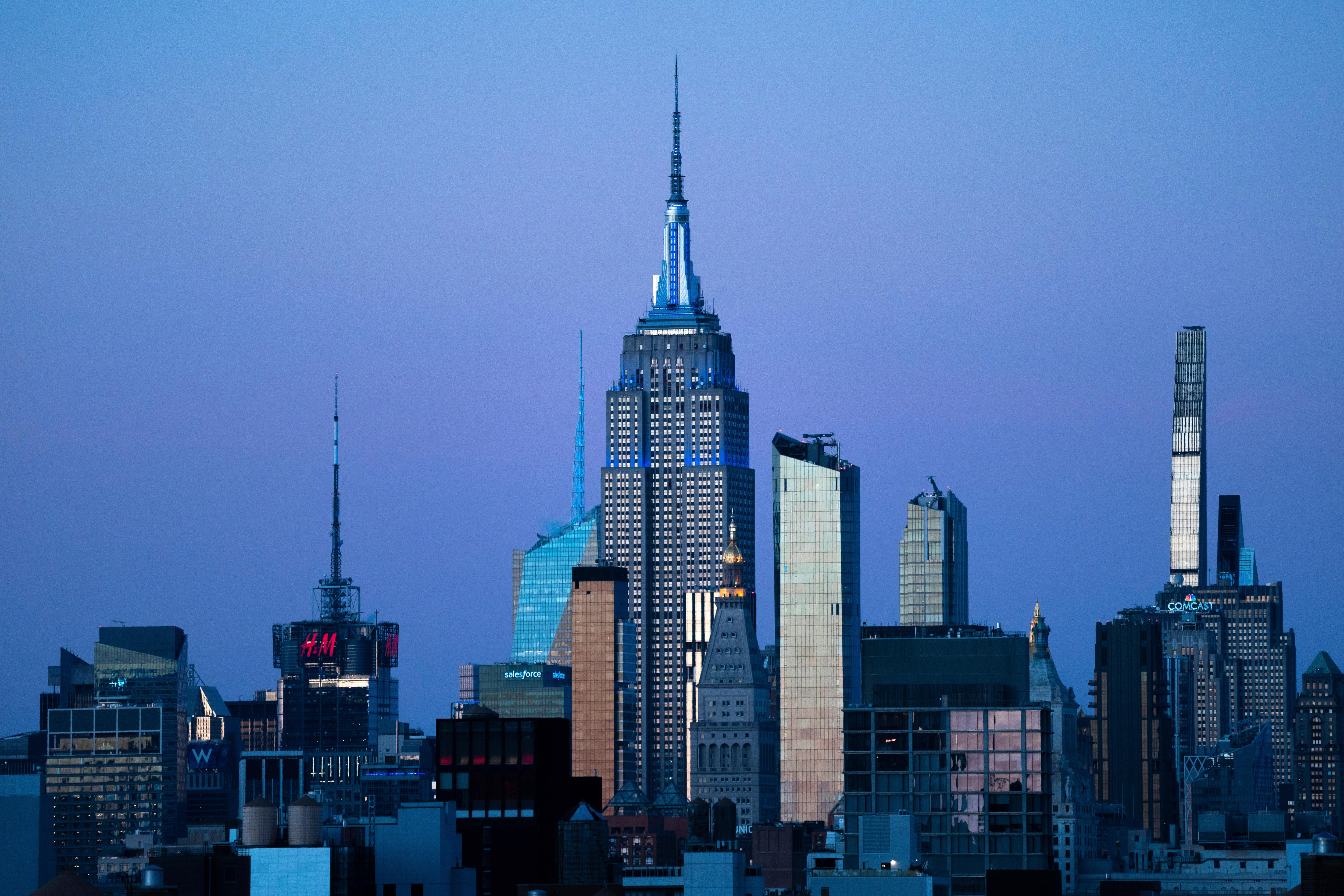 The new York City skyline, including the Empire State Building shown centre, at dusk in a blue-purple sky light.
