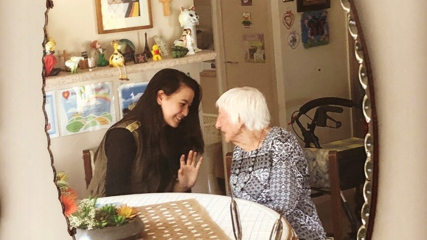 Hasinah Zainal and Peggy Muller sitting at a table in her unit in Brisbane, with image capture in a mirror.