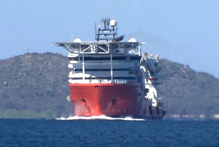 A front-on view of a red and white commercial ship with hills in the background.