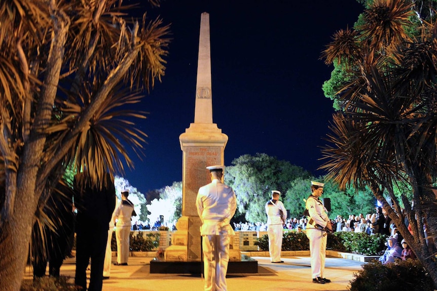 Soldiers in white stand near a war memorial during a dawn service.